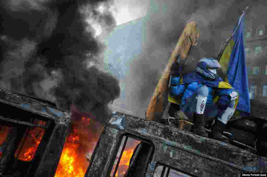 A protester protects himself from a fire as he sits on the roof of a burned-out bus in downtown Kyiv.