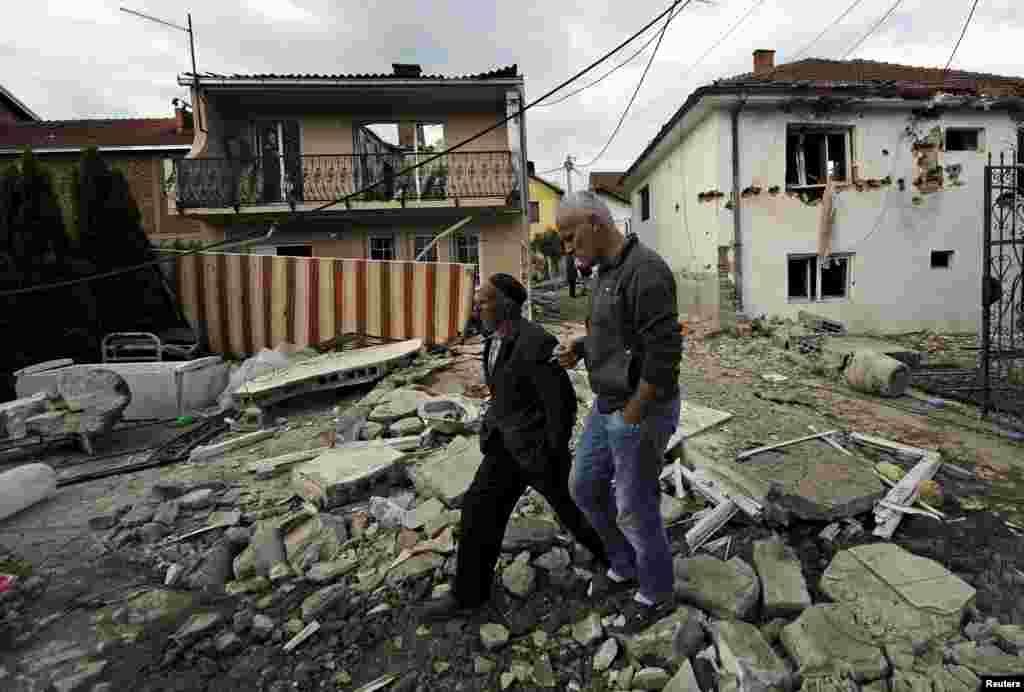 People walk past houses damaged in the gunbattle in Kumanovo.