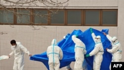 Japanese Self-Defense Force officers in radiation-protection suits hold a blue sheet over patients who were exposed to high levels of radiation at the Fukushima nuclear power plant as they are transferred to a hospital on March 25.