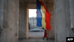 A woman walks under the Triumph Arch next to Moldovan flag on Stefan Cel Mare street in Chisinau. (file photo)