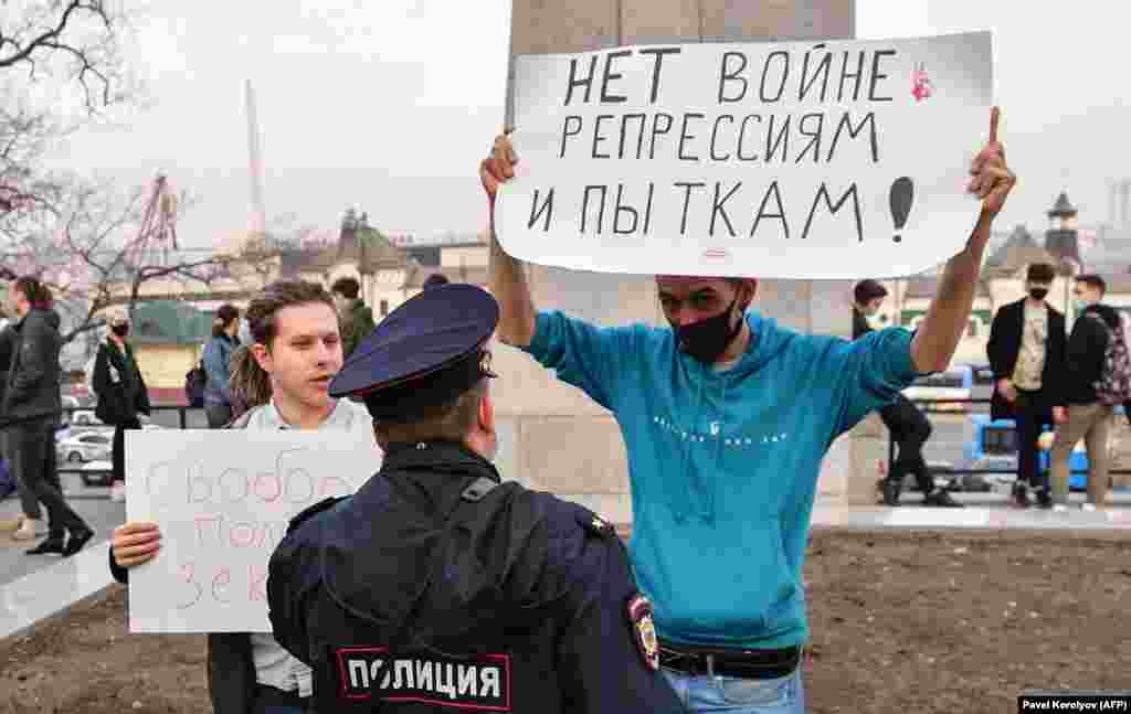 A police officer speaks with an opposition supporter holding a poster reading &quot;No war, repression, and torture!&quot; at the rally in Vladivostok.