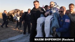 Ground personnel carry ISS crew member Drew Feustel of the United States shortly after landing in a remote area of Kazakhstan on October 4. The Soyuz capsule can be seen in the background.