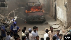 Onlookers gather near a burning vehicle in a troubled area of Karachi