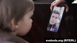 The 2-year-old daughter of imprisoned Belarusian blogger Ihar Losik looks at her father's photograph on the mobile phone of his wife, Darya Losik.