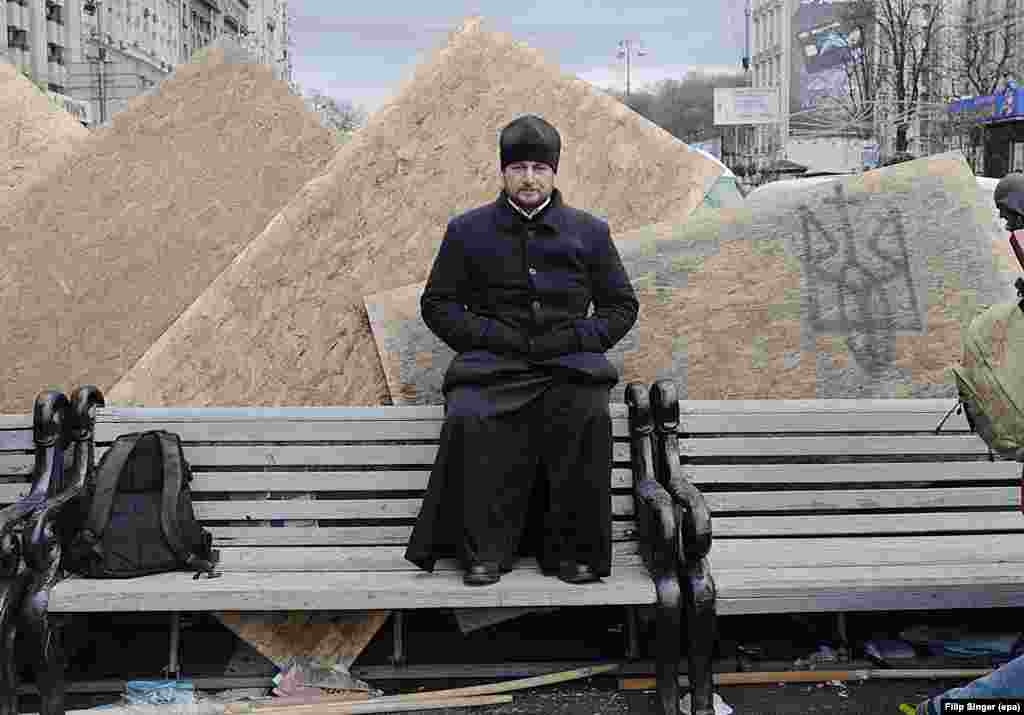 An Orthodox priest sits on a bench at Kyiv&#39;s Independence Square.