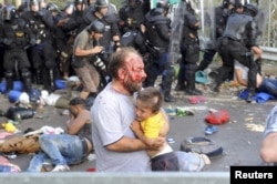 An injured migrant carries a child during clashes with Hungarian riot police at the border crossing with Serbia in Roszke on September 16.