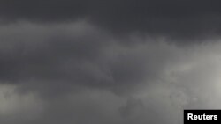 A Greek flag flies under a cloudy sky in Athens.