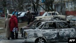 People look at burned-out cars as they walk along a street in the southern Ukrainian city of Mariupol, which was heavily shelled on January 24. 