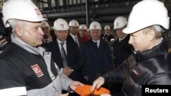 Prime Minister Vladimir Putin (right) dips his hand into a hardhat full of oil. Critics say he's likely delighted by international crises that have increased the value of Russia's chief export.