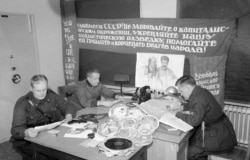 Finnish officers with seized Soviet propaganda. The banner says, "Workers of the U.S.S.R.! Do not forget about capitalist encirclement. Strengthen our socialist intelligence [service and] help it destroy and uproot enemies of the people!"