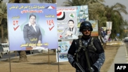 An Iraqi security officer patrols a street past provincial election posters.