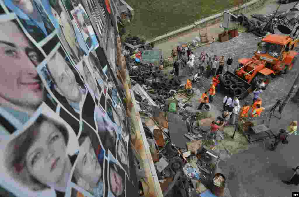 Pictures of people who were killed during the winter protests are attached to a bridge as municipal workers clean up a barricade on Independence Square in Kyiv on&nbsp;August 11, 2014. The downtown area of the Ukrainian capital was reopened after citizens had cleaned up the central streets two days previously.