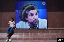 An Afghan boy sits next to poster bearing the image of the late resistance leader Ahmad Shah Masud.