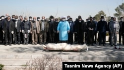 Mourners wearing face masks and gloves pray over the body of a former official in the Islamic Revolutionary Guards Corps, Farzad Tazari, who died on May 9 after being infected with the new coronavirus, at the Behesht-e-Zahra cemetery just outside Tehran on March 10.