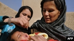 An Afghan woman holds a child as a health worker administers the polio vaccine. The WHO says that large-scale immunization can stop an outbreak.