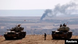 Turkish tanks near the Syrian border look on as smoke rises from the besieged city of Kobani on October 8.