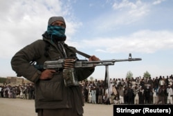 A member of the Taliban and onlookers stand at the site of the execution of three men convicted in a Taliban shadow court in Ghazni Province.