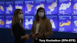 Women standing near a digital board displaying preliminary voting results from Russian regions at the Central Election Commission information center in Moscow. 