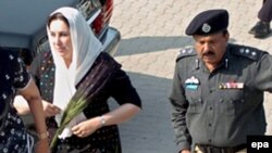 A police officer escorts Benazir Bhutto (left) as she visits a national shrine in Karachi in October 2007.