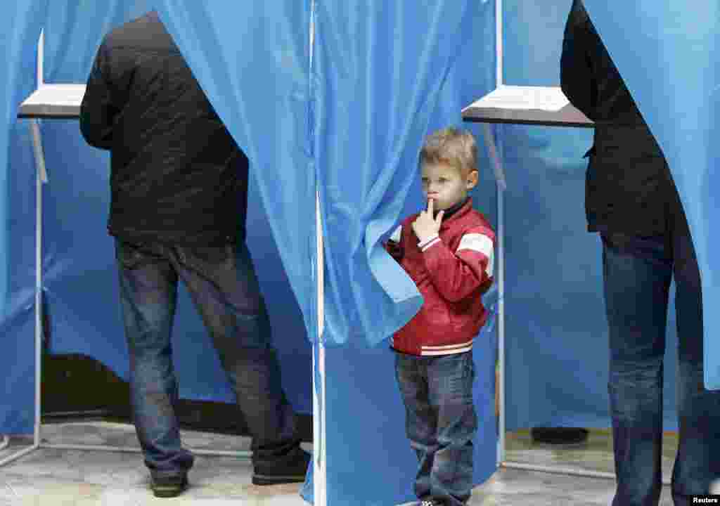 A boy peers around the curtain of a voting booth at a polling station in the capital, Kyiv. (REUTERS/Gleb Garanich)