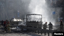 Ukrainian servicemen and first responders stand by a damaged vehicle in Kyiv on February 26.