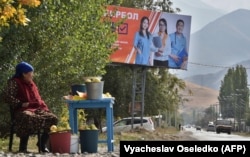 A woman sells fruit on the side of a road in front of a campaign billboard for the Bir Bol (Stay Together) party in the village of Koy-Tash, some 20 kilometers from the capital, Bishkek, on September 30.