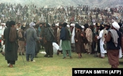 Taliban fighters gather around surgeons cutting off a thief's hand in Kabul's national stadium. (file photo August 1998)