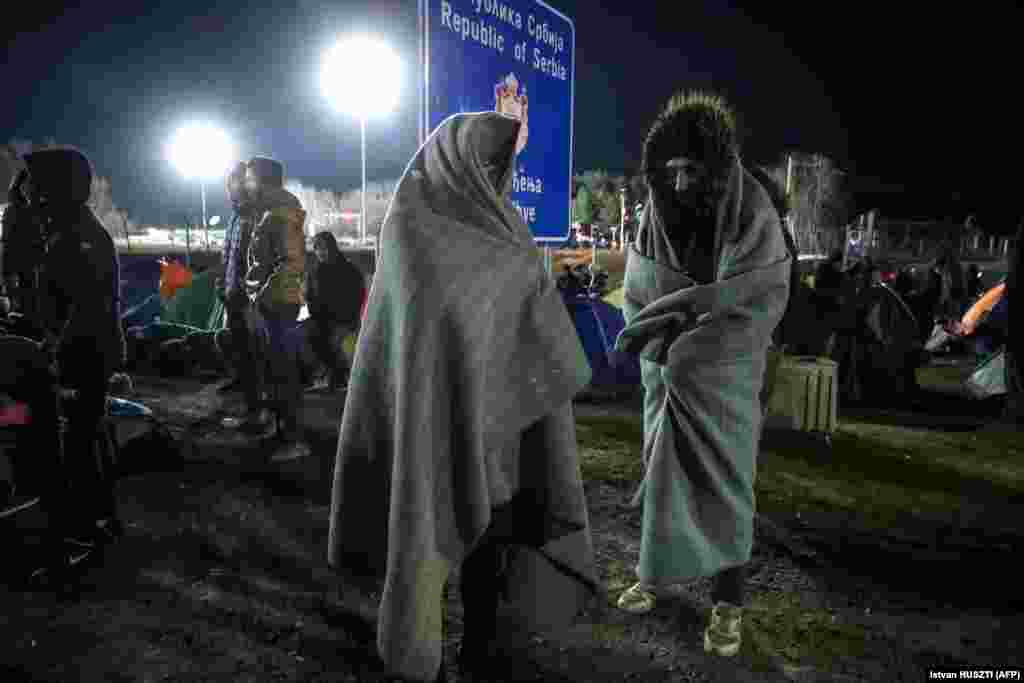 Migrants stand wrapped in blankets near the border fence at the Serbian border village of Kelebija, near Subotica, on February 6.