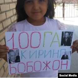 A young girls holds up a sign saying she hopes the Uzbek president lives to be a hundred.