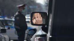 A person wearing a protective mask is reflected in the side mirror of a car near a Kazakh police officer in Almaty.