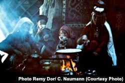 A nomadic Pamir Kyrgyz family gathers around an open-fire stove inside their yurt.