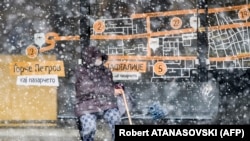 A woman waits for public transport at a bus stop during heavy snowfall in Skopje on April 1.