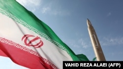 An Iranian flag flies at an undisclosed location in the Islamic republic next to a surface-to-surface Qiam-1 missile. (file photo)