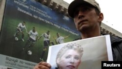 An opposition supporter holds a photo of former Prime Minister Yulia Tymoshenko in front of a billboard for Euro 2012 in Kyiv.