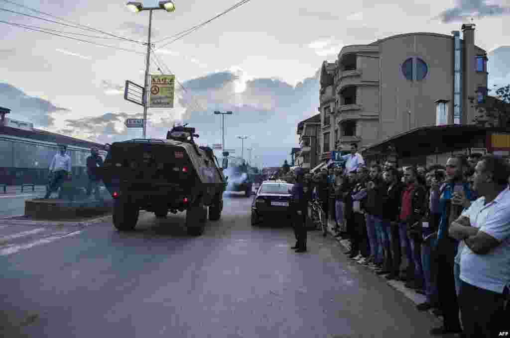 People watch as Macedonian police troops in armored vehicles leave the area where fighting took place in Kumanovo.