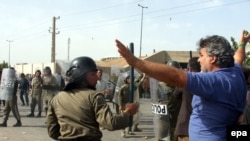 An Iranian riot police officer raises a baton toward protesters during the mourning ceremony at the Behesht Zahra Cemetery on July 30.