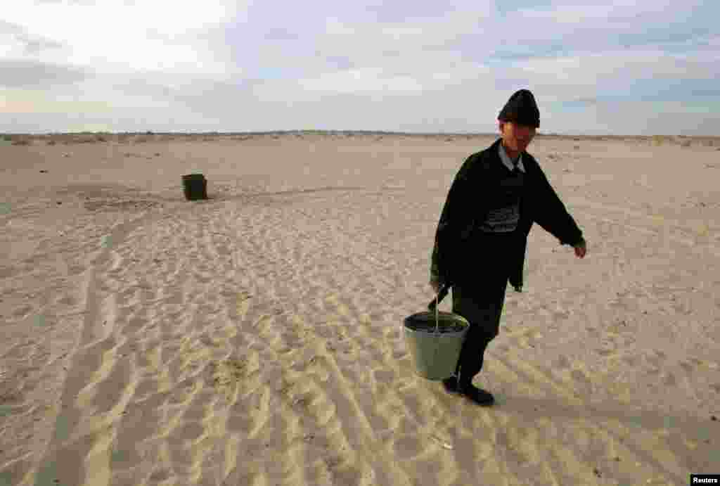 A Kazakh villager carries a bucket of water from a well in a desert that once formed the bed of the Aral Sea.