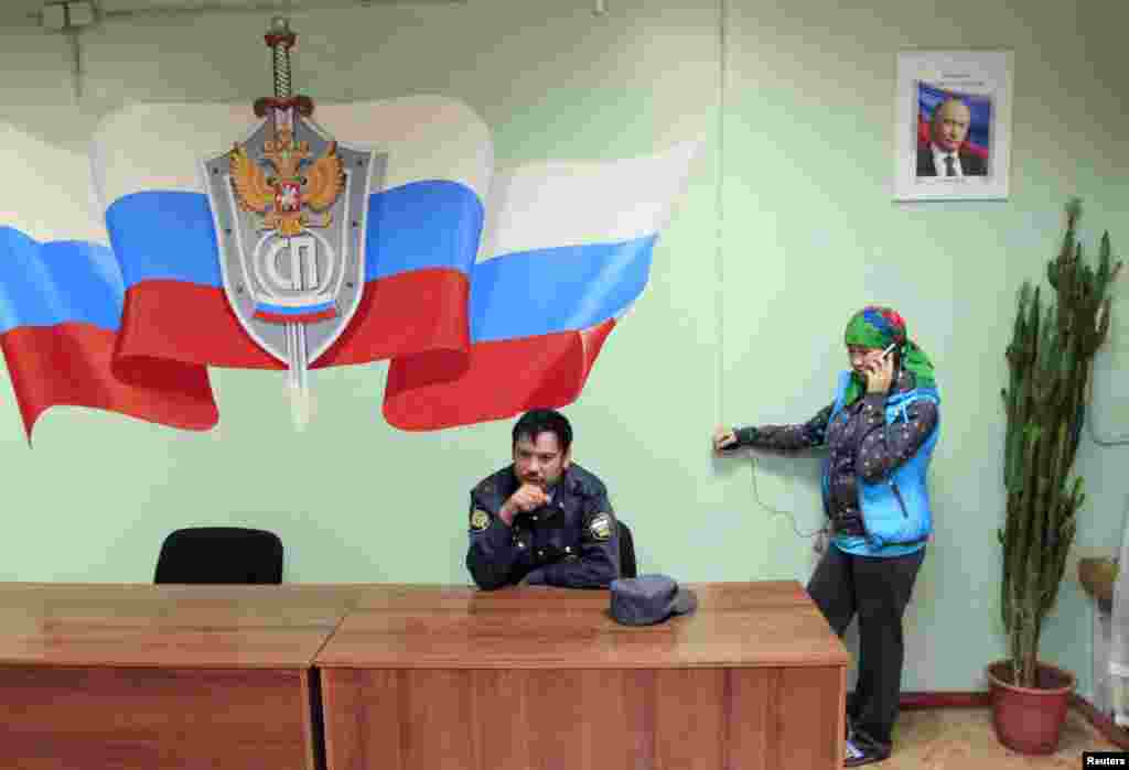 A police officer in Krasnoyarsk waits as a detained illegal migrant from Central Asia makes a telephone call before being deported in September 2013.&nbsp;