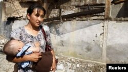 An ethnic Uzbek woman and her child, just returned to Osh from Uzbekistan, walks past a house that was burned down during ethnic clashes.