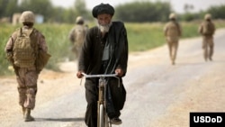 An Afghan man rides through the Nawa District bazaar past a security patrol by U.S. Marines and Afghan soldiers in Helmand Province.