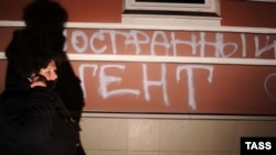 A man walks past graffiti spray-painted on the building used by the Memorial human rights group. It reads: "Foreign agents. I love USA."