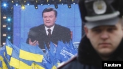 Supporters of President Viktor Yanukovych wave flags beneath a screen showing his live televised question-and-answer session as a policeman keeps watch in central Kyiv on February 25.