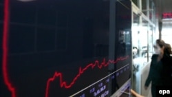 A woman walks next to an electronic board recording the indicator of a session at the stock exchange in Athens on November 1.