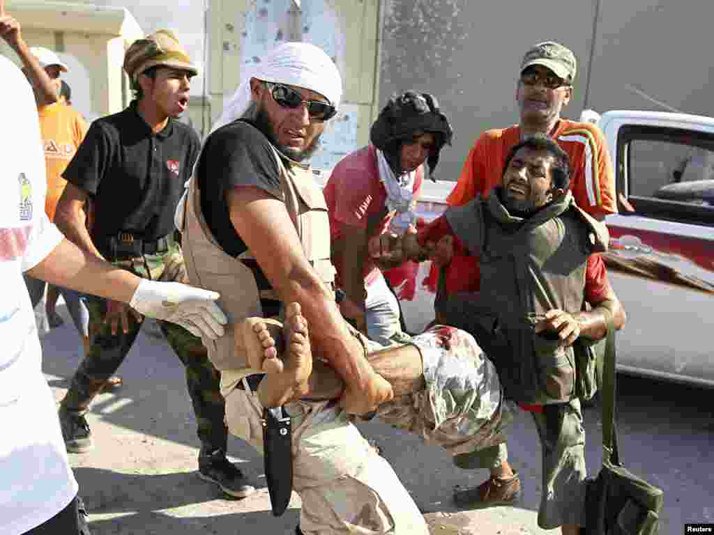 Libyan rebel fighters carry a wounded comrade near the gates of Qaddafi's Bab al-Aziziya stronghold.