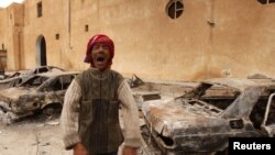 A man stands in front of burnt vehicles outside a state security building in Tobruk, east of Libya.