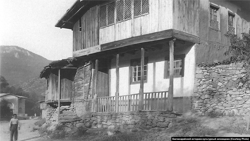 A house in southwestern Crimea, 1920s. The standard interior of the main room included an open fireplace with a chimney and a cauldron suspended from it on a chain. Along the walls, there were low sofas with mattresses and pillows. Numerous towels were used to decorate the walls, and there were carpets on the floor.