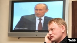 Former police major Aleksei Dymovsky speaks on the phone while President Vladimir Putin appears on television.