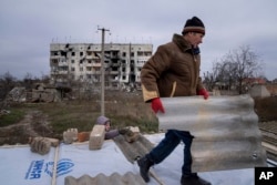 A man helps his neighbor to repair a roof after their houses were destroyed during fighting between Russian and Ukrainian forces in the recently retaken town of Arhanhelske earlier this month.