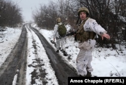 A soldier gestures to a photographer to keep to one side of the road to avoid being targeted by a potential sniper.