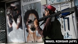 A Taliban fighter walks past a beauty salon with images of women defaced using spray paint in Kabul on August 18, days after the militant group seized the Afghan capital. 